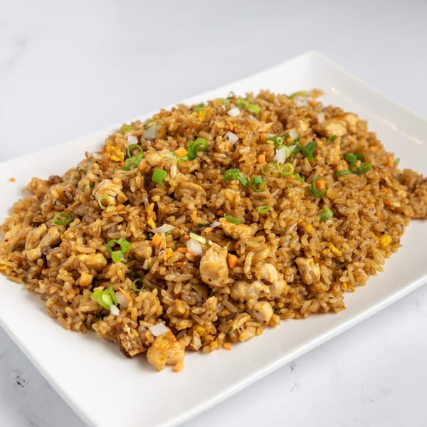 A large serving of chicken fried rice with chopped scallions and vegetables on a white rectangular plate.