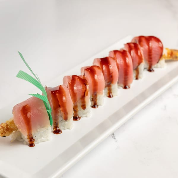 Jojo Japanese Hibachi & Sushi's tuna sushi roll, topped with sauce and green garnish, on a white plate.