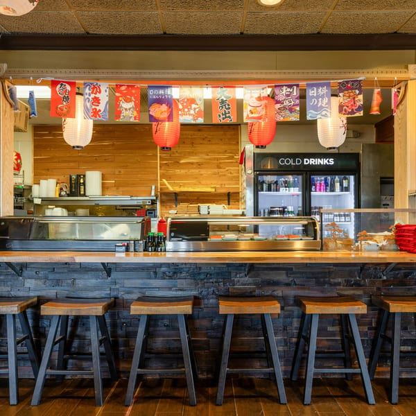 Sushi bar with wooden stools, paper lanterns, and Japanese banners at Jojo Japanese Hibachi & Sushi.