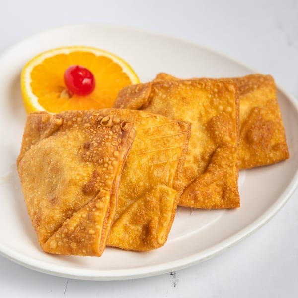 Golden-fried crab rangoons on a white plate, garnished with an orange slice and a maraschino cherry.
