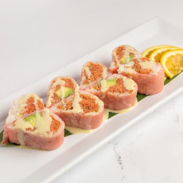 Six heart-shaped sushi rolls with avocado and spicy tuna, drizzled with sauce, on a white plate.