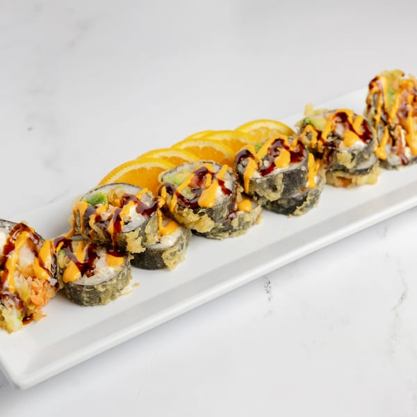 Deep-fried sushi rolls with orange and brown sauces, garnished with orange slices on a white platter.
