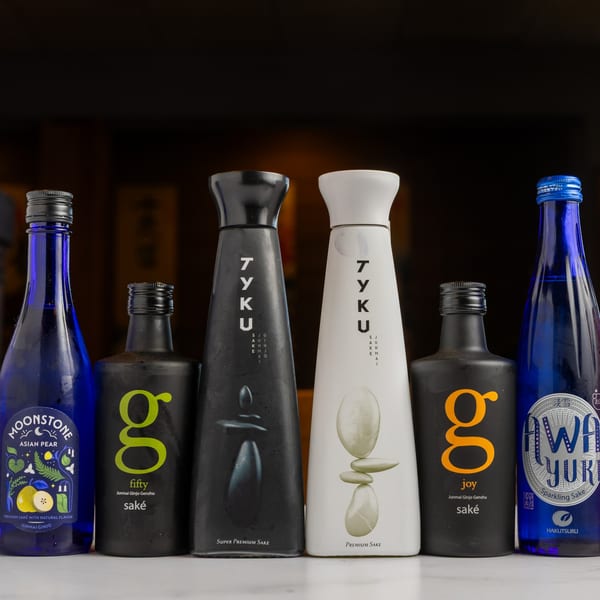 A row of six diverse sake bottles, including blue, black, and white designs, on a white surface.